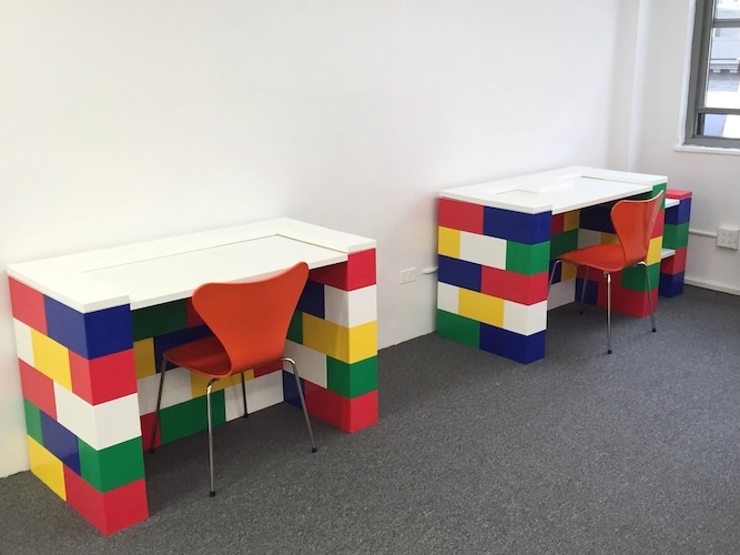 Two white desks built with colorful modular blocks, each paired with an orange chair