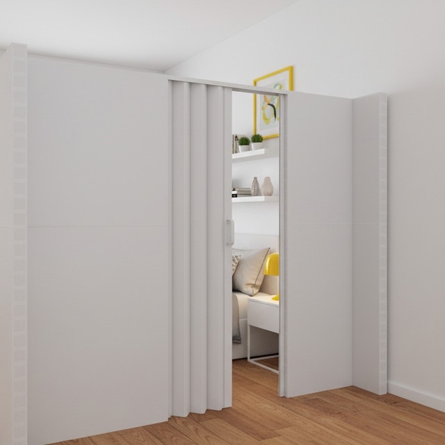 Modern white room divider with an integrated accordion door, creating a private bedroom nook in a bright, minimalist interior with wood flooring and built-in shelving.