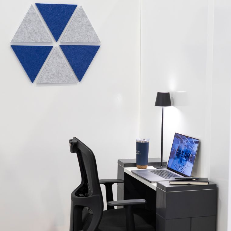 Minimalist office nook with a desk, laptop, task lamp, and blue-and-gray geometric acoustic wall panels.