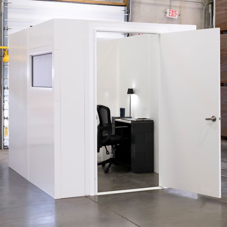 White modular privacy room with an open door revealing a small desk, chair, and task lamp