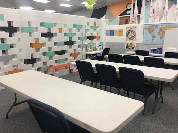 Classroom with white tables, black chairs, and a colorful modular block partition wall.