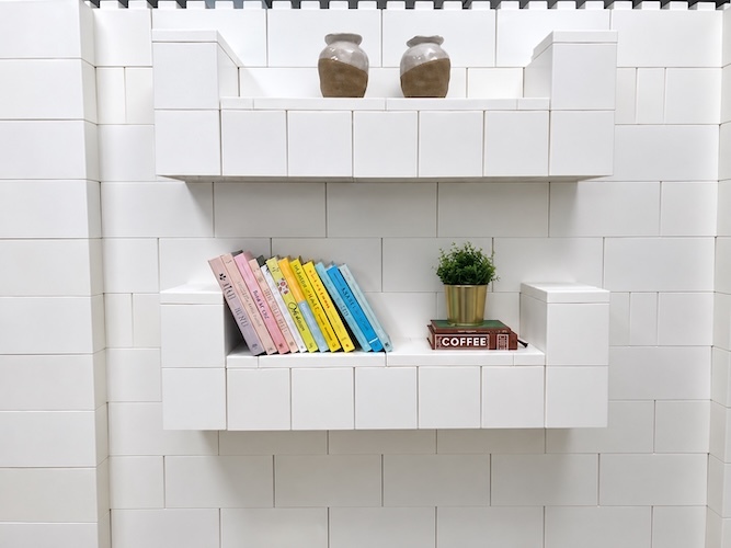 White modular block wall with built-in floating shelves displaying colorful books, plants, and decorative vases.