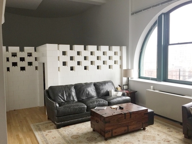 White staggered-block wall divides a loft living room with a leather sofa and coffee table.